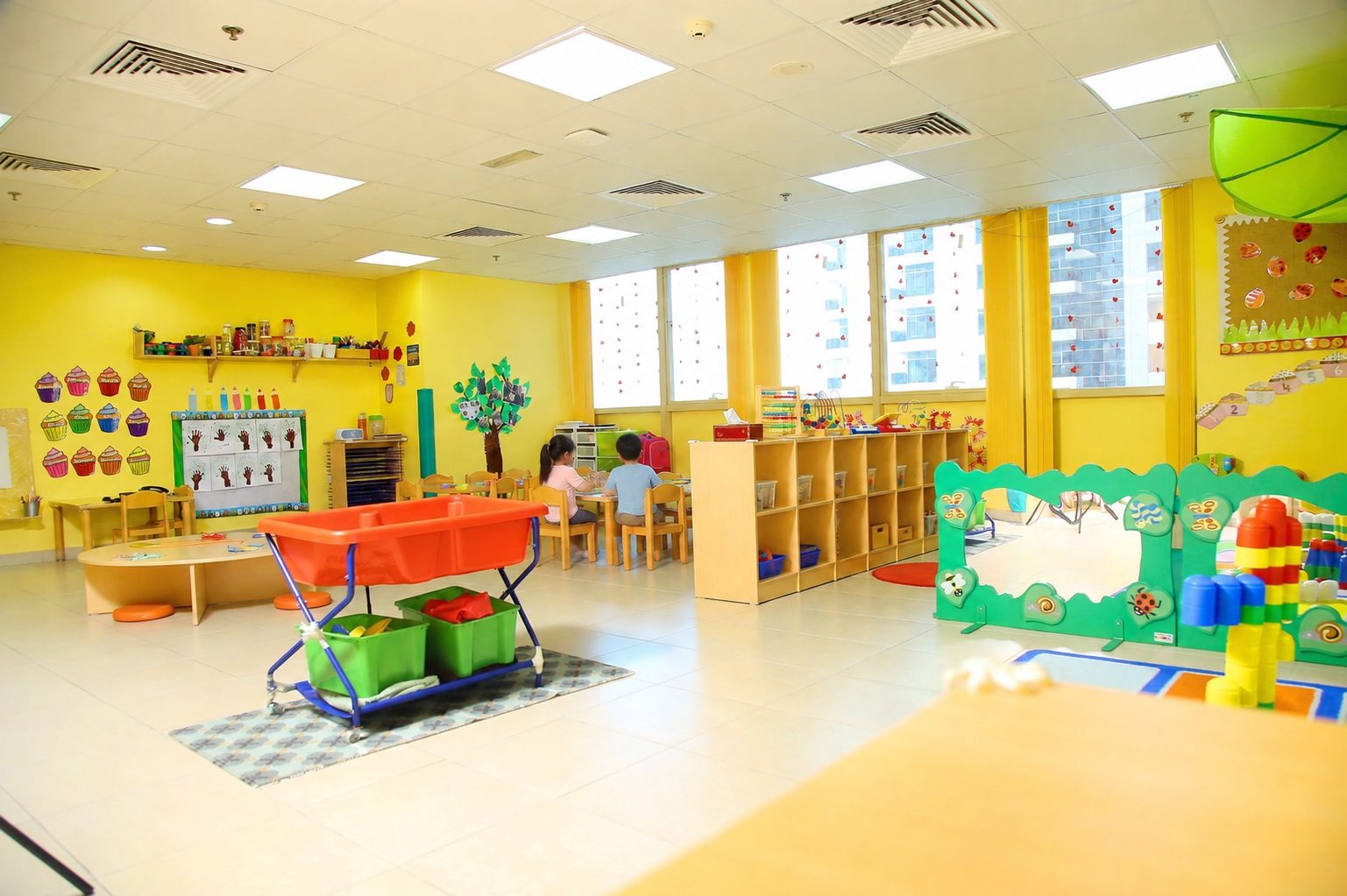 The Toddlers room, with a water tray on a trolley, low shelving of labelled trays and a soft play divider