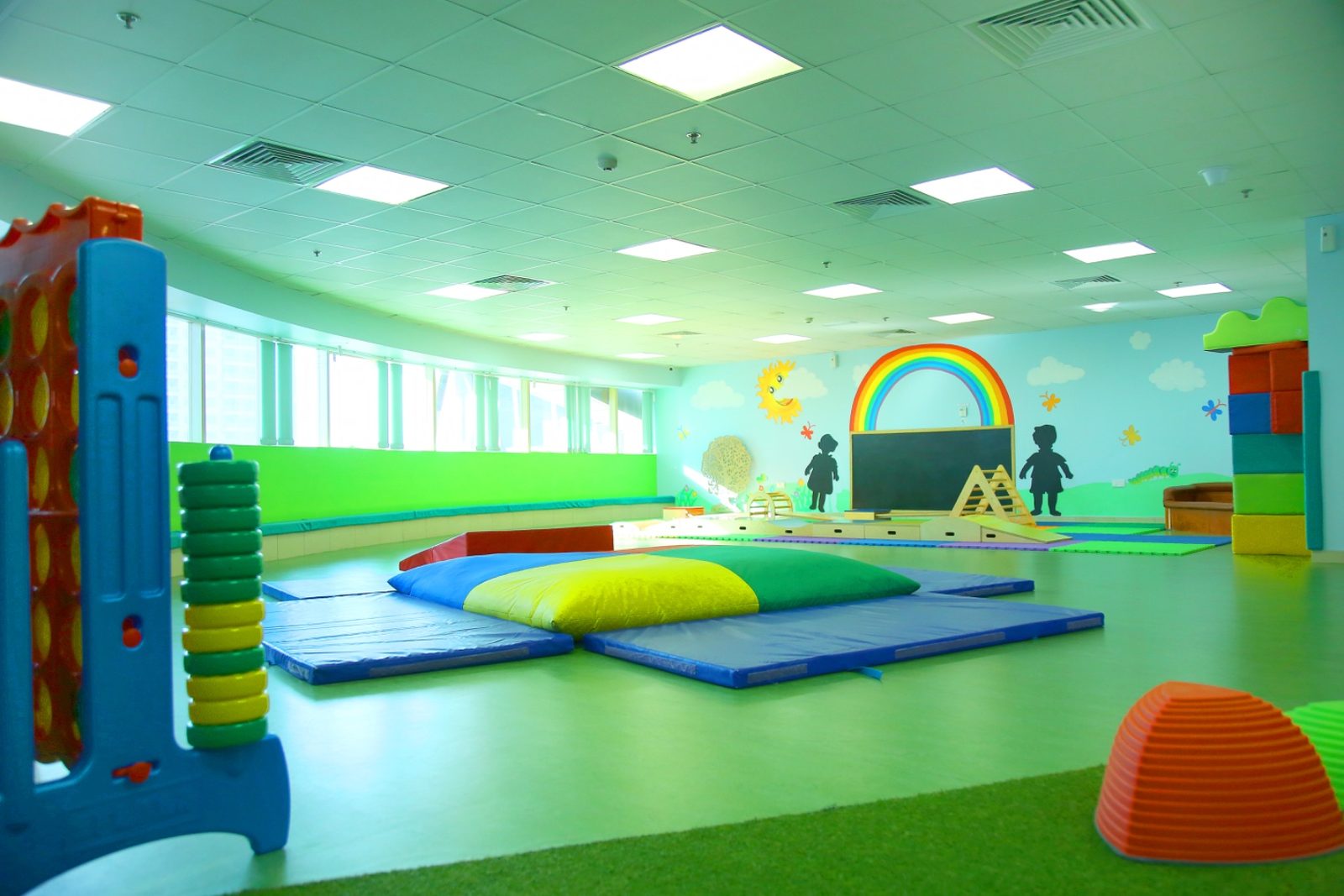 The indoor soft-play hall, with crash mats, a large soft wedge and foam climbing blocks on a green floor